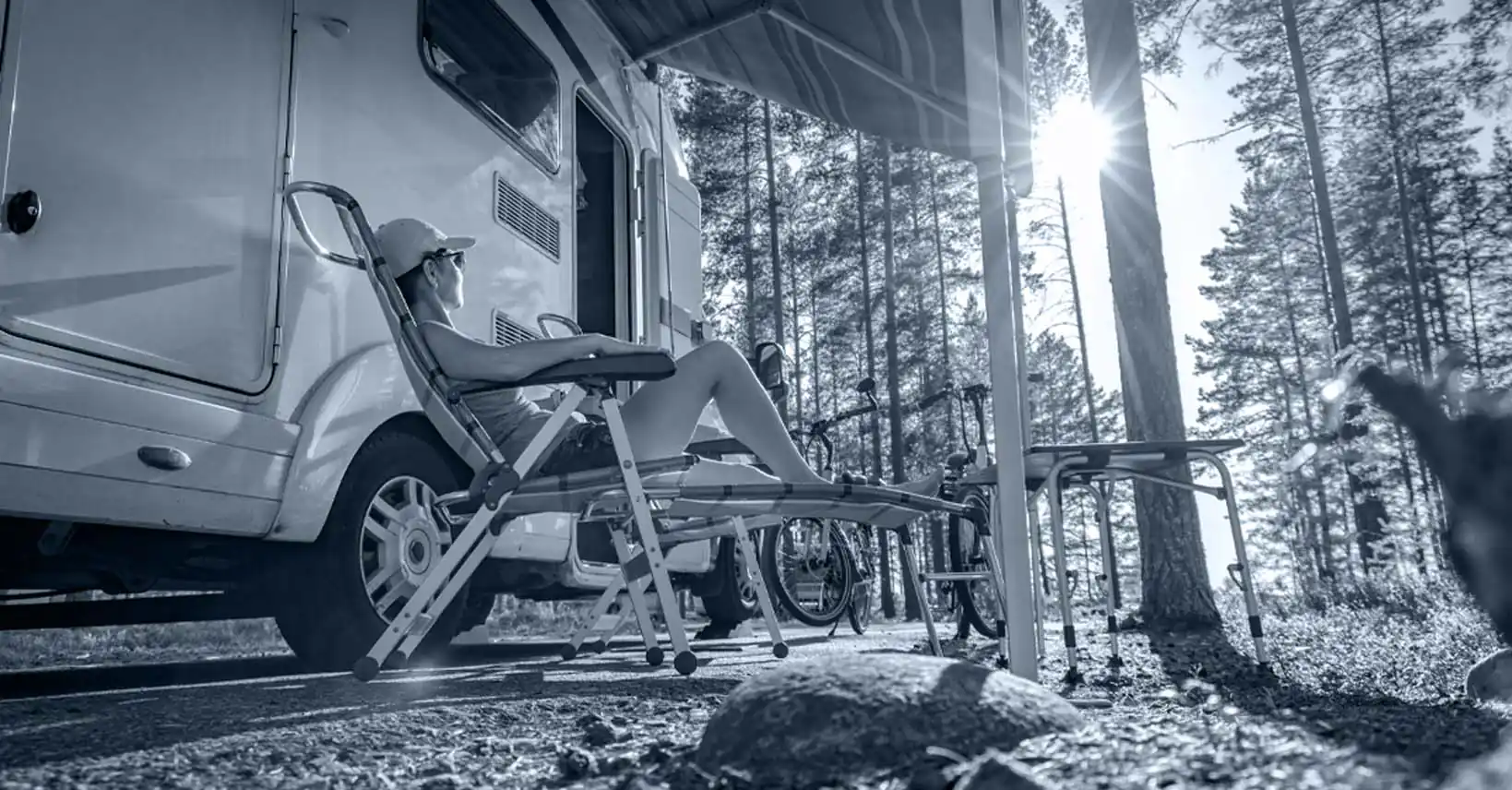 Camper relaxing in a lawn chair beside an RV in the woods